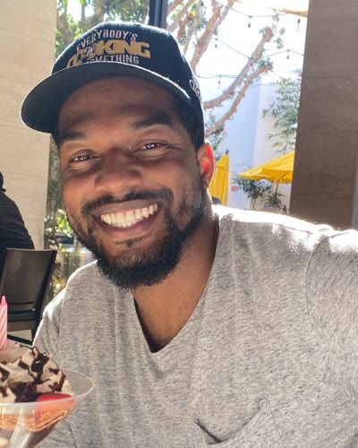 Chandler smiling at a restaurant table, wearing a black cap